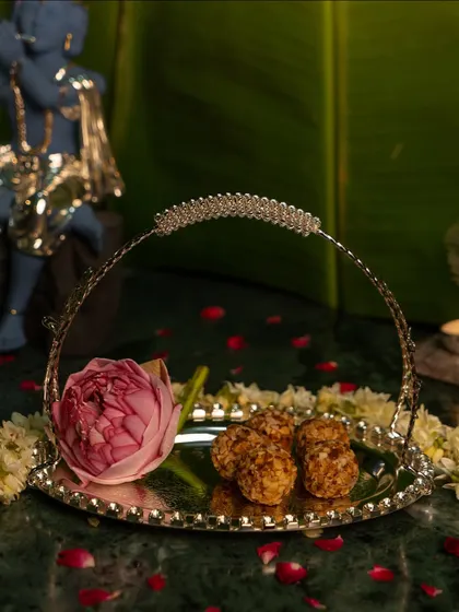 Divine offerings for Shri Krishna this Janmashtami. A silver basket tray holds sweets and a lotus flower, creating a beautiful and devotional offering for the festive celebration.