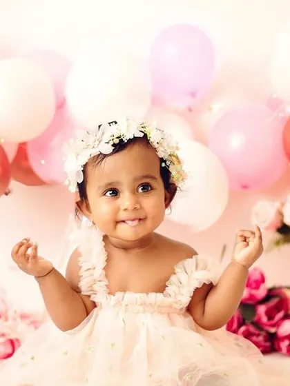 A beautiful pre-cake-smash portrait for a little girl. The pink balloons, roses, and floral crown create a soft and celebratory atmosphere.