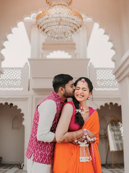 A sweet kiss on the cheek. This candid moment during their Haldi photoshoot is full of affection and the bride's genuine, happy scrunch-nosed smile.