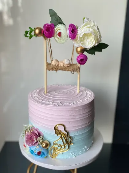 A dreamy baby shower cake with a mermaid and baby-on-a-swing theme. The pink and blue ombre frosting and delicate floral details make it truly magical.