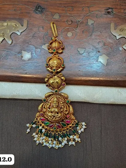 This lightweight maang tikka is made from hallmarked 92.5 silver with gold plating. It features a Goddess Lakshmi motif and is adorned with colorful stones and pearl drops.