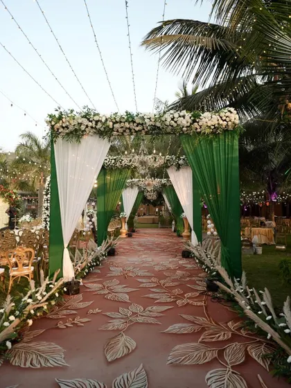 A stunning entrance walkway for a wedding ceremony. The combination of green and white drapes, a floral-printed carpet, and elegant chandeliers creates a grand and welcoming path for guests.