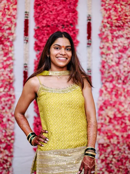 The bride posing confidently against a floral wall at her Haldi ceremony.