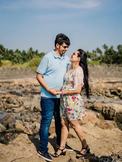 A happy couple posing on the rocks by the sea, a perfect example of a daytime beach pre-wedding photo.