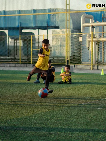 A young player practices their shooting technique, with teammates watching in the background. Our sessions are structured to keep all players engaged.
