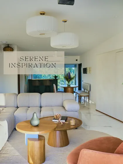 An open-plan living space designed for serenity and flow. The large, comfortable sectional sofa, paired with organic-shaped wooden coffee tables and soft, pleated pendant lights, creates a cohesive and tranquil environment.