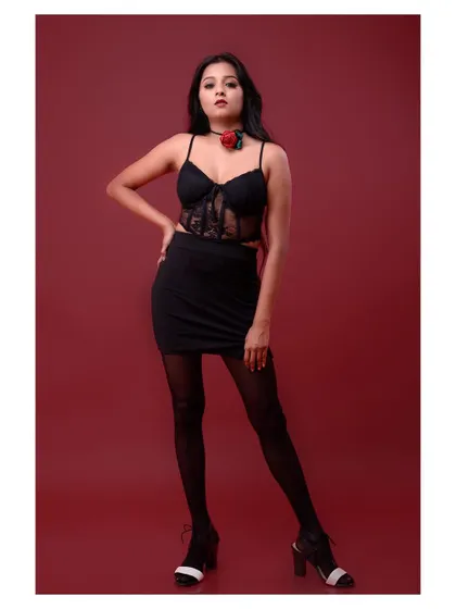 A full-body shot of a model in a black dress against a red background. The pose is strong and confident, creating a classic and powerful fashion statement.