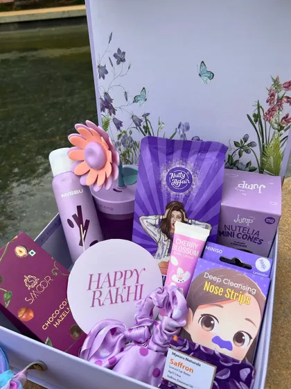 A gorgeous purple-themed Rakhi hamper for a sister. It's packed with beauty products, a cute scrunchie, and chocolate, all in shades of purple.