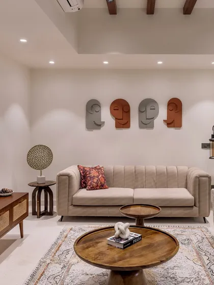 This contemporary living room from 'Project Lily' showcases a mix of earthy tones with a comfortable beige sofa, a wooden TV console with cane detailing, and artistic face sculptures on the wall.