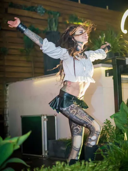 The female Steampunk artist in a joyful, dancing pose. Her costume features custom body art and a mix of leather and lace elements.