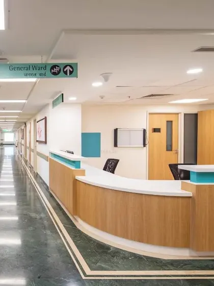 This corridor at a Max Healthcare facility features clear wayfinding signage and a clean, uncluttered design. The layout simplifies navigation for patients and optimizes workflow for staff by standardizing the location of utility areas.