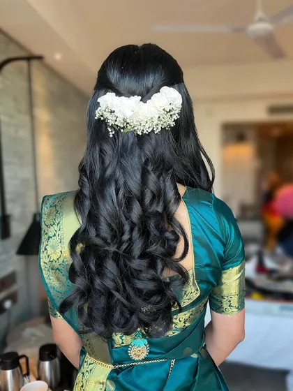 A view of the beautiful half-up hairstyle with voluminous curls and fresh white flowers. This hairstyle is a modern take on a traditional look.