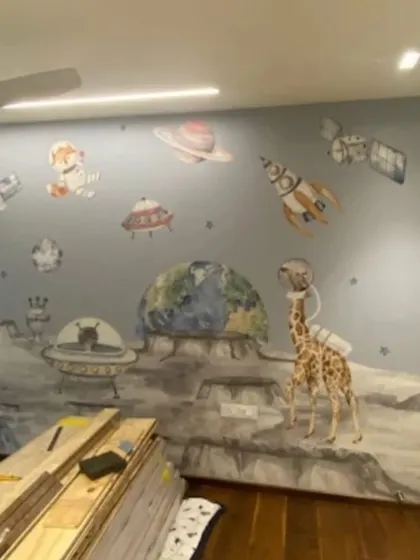 An imaginative outer space mural where a giraffe in an astronaut helmet explores the moon, blending fantasy and science for a unique kids' room.