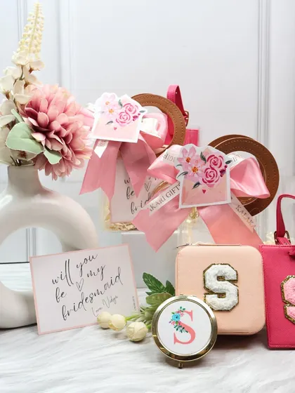 A bridesmaid proposal hamper in a chic pink theme. This set includes a personalized jewelry case and luggage tag, a custom pocket mirror, and a "Will you be my bridesmaid?" card, all beautifully arranged.