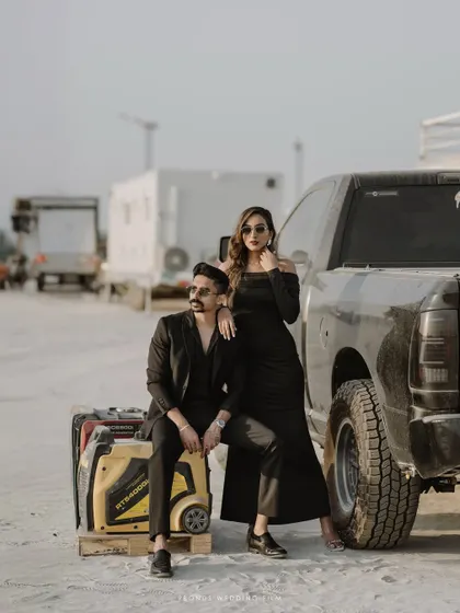 A full-length shot of the couple's edgy, high-fashion pose by a truck, showcasing their confidence and the unique industrial-desert setting.