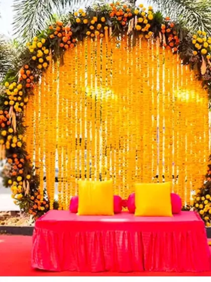 Our most requested Haldi backdrop design. A large ring of marigolds frames a curtain of genda strings, with a simple diwan for seating, perfect for any outdoor pre-wedding event.
