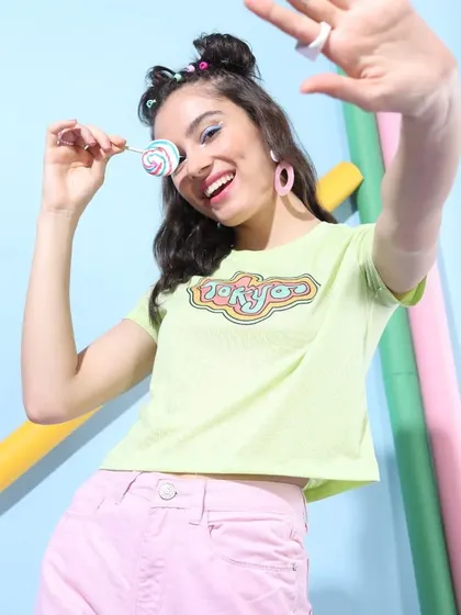 A bright, summery look featuring a lime green graphic tee and pink denim, with a small lollipop prop to add a touch of sweetness.