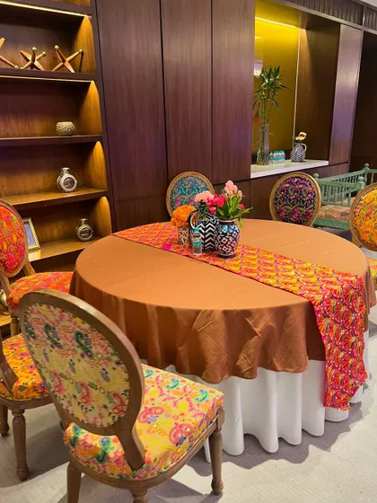 Guest dining table setup for a luxury Mehendi. The chairs are upholstered in a vibrant, traditional print, and the table features a matching runner.