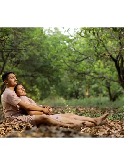 A couple relaxes together on a bed of fallen leaves in a forest, holding each other in a peaceful and natural embrace.