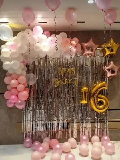 A sweet 16th birthday party with a pink and white balloon garland against a silver shimmer curtain.
