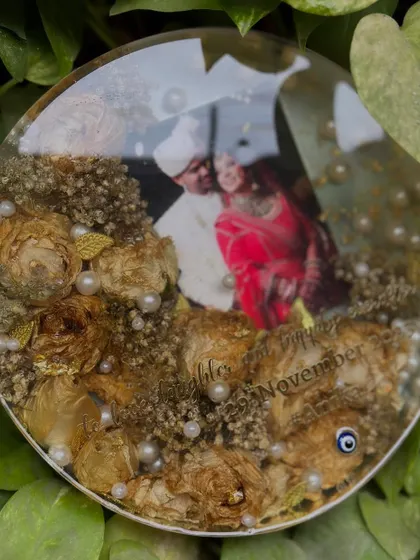 A favorite from this year. This circular keepsake beautifully preserves a couple's wedding photo and varmala flowers, with delicate pearls and a nazar battu for blessings. The clarity of the resin makes the memories pop.