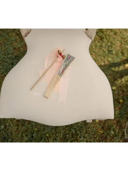A simple, elegant detail for guests at a garden wedding. A hand fan and a bell wand are placed on each chair, providing comfort for the sunny ceremony and a way for guests to joyfully cheer for the couple.