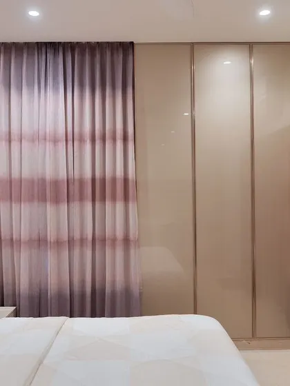 A detail shot of the mauve bedroom, showing the clean lines of the back-painted glass wardrobe next to the textured curtains.