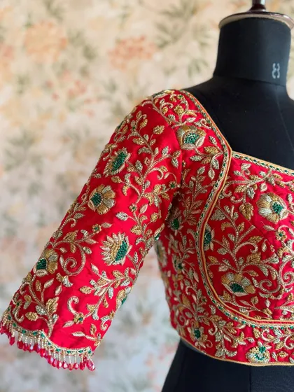 A close-up of the sleeve on a red bridal blouse. The dense floral and vine pattern is a classic choice for wedding wear.