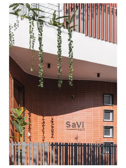 The entrance of the 'SaVi' residence, also known as the 'House Under Tabebuia Trees', features a curved cantilevered roof with hanging plants, welcoming you into a space where architecture and nature meet.