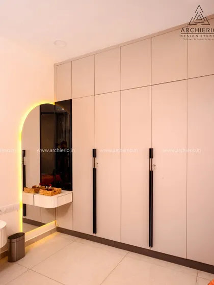 A minimalist wardrobe with an integrated vanity and an arched, backlit mirror, creating a sleek and functional getting-ready corner.
