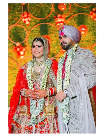 The couple stands together, smiling, against a vibrant, lit-up backdrop. This image captures the celebratory atmosphere of their wedding night.