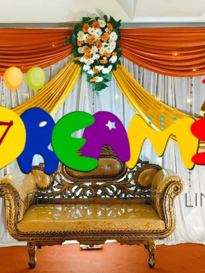 This is a classic reception stage design using rich fabric drapes in orange and white. The setup is completed with a golden sofa and four large floral bouquets that frame the stage.