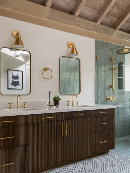 The double vanity in the Saratoga master bathroom, featuring dark wood cabinetry, a white marble countertop, and elegant brass fixtures. The design is clean and modern, yet the materials add a sense of warmth and timeless luxury.