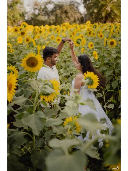 A playful moment during a pre-wedding shoot in a sunflower field, with the couple dancing among the tall, bright flowers.