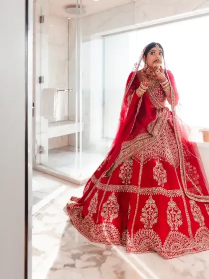 The bride, in her stunning red lehenga, strikes a playful pose in a modern bathroom. This fun, unconventional shot shows her personality shining through even in a traditional outfit.