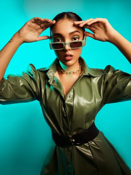 A high-fashion look featuring a green leather jacket and statement sunglasses. I used a vibrant aqua-colored background to make the olive green pop, creating a modern and edgy fashion portrait.