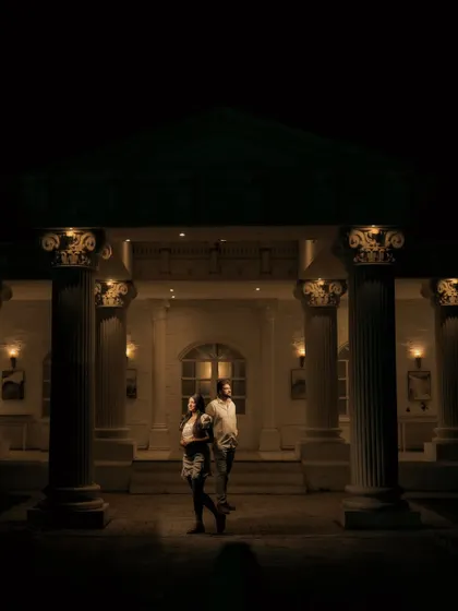 A dramatic, wide-angle shot of a couple in front of a grand, columned building at night, creating a cinematic and timeless feel.