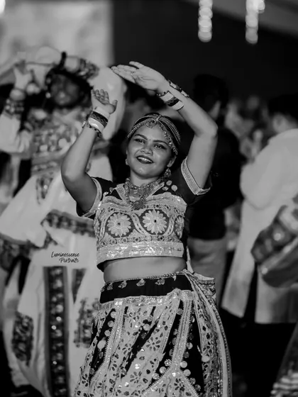 A black and white shot of a woman dancing, her hands raised in a classic Garba pose, her happiness evident.