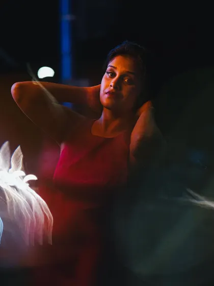 An abstract and colorful night portrait with creative light flares obscuring parts of the image. The model's direct gaze cuts through the blur, creating a mesmerizing and artistic effect.