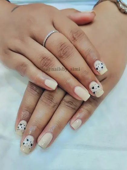 A nude base gel polish with small, freehand black hearts on the accent nails.