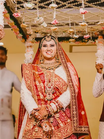A beautiful, happy bridal portrait taken during the wedding ceremony. Her candid expression and the traditional red and white attire make for a joyful and authentic image.