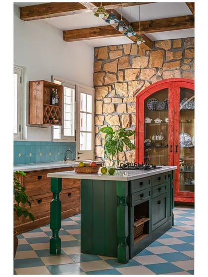 The "Far from the Stone Street" kitchen, a maximalist's dream with its stone wall, checkerboard floor, and bold green, red, and blue cabinets.