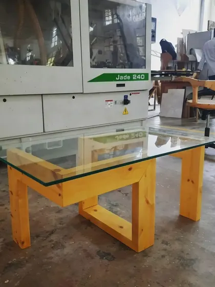 A modern coffee table with a glass top and a geometric pinewood base, showcasing the students' ability to combine different materials into a finished piece.