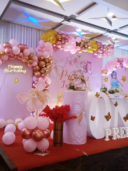 A pretty pink fairy theme for baby Preksha's first birthday. The setup includes a full stage with pink backdrops, a rose gold and pink balloon garland, and a "ONE" table for the cake.