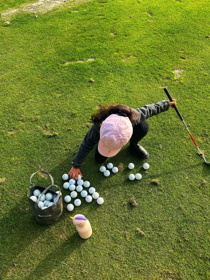 A young golfer gathers her practice balls on the green, ready for another round of drills.