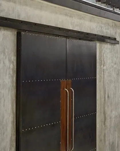 A detail of the industrial-style sliding door at the Automobile Design Studio. The combination of raw steel, precise riveting, and warm wooden handles exemplifies our approach of blending robust materials with thoughtful, human-centric details.