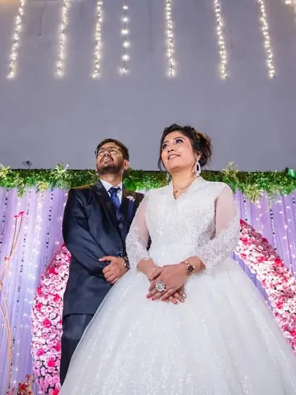 A grand, wide shot of the couple on their beautifully decorated reception stage, looking up at the lights.