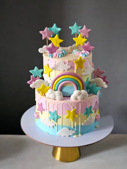 A dreamy pastel-colored cake with a "Twinkle Twinkle Little Star" vibe. This two-tiered cake is decorated with fondant stars, clouds, and a rainbow, with a gentle drip effect.