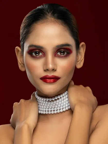 A bold beauty portrait defined by its striking red eyeshadow and glossy lips. The clean composition and pearl choker draw all attention to the model's intense expression.