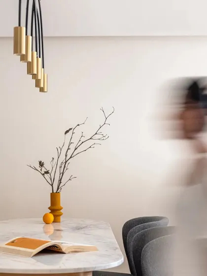 A minimalist detail of the dining table, focusing on the simple, elegant forms and the interplay of light from the modern fixture.